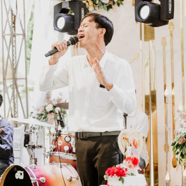 Singer performing with a handheld microphone at a wedding reception with a live band